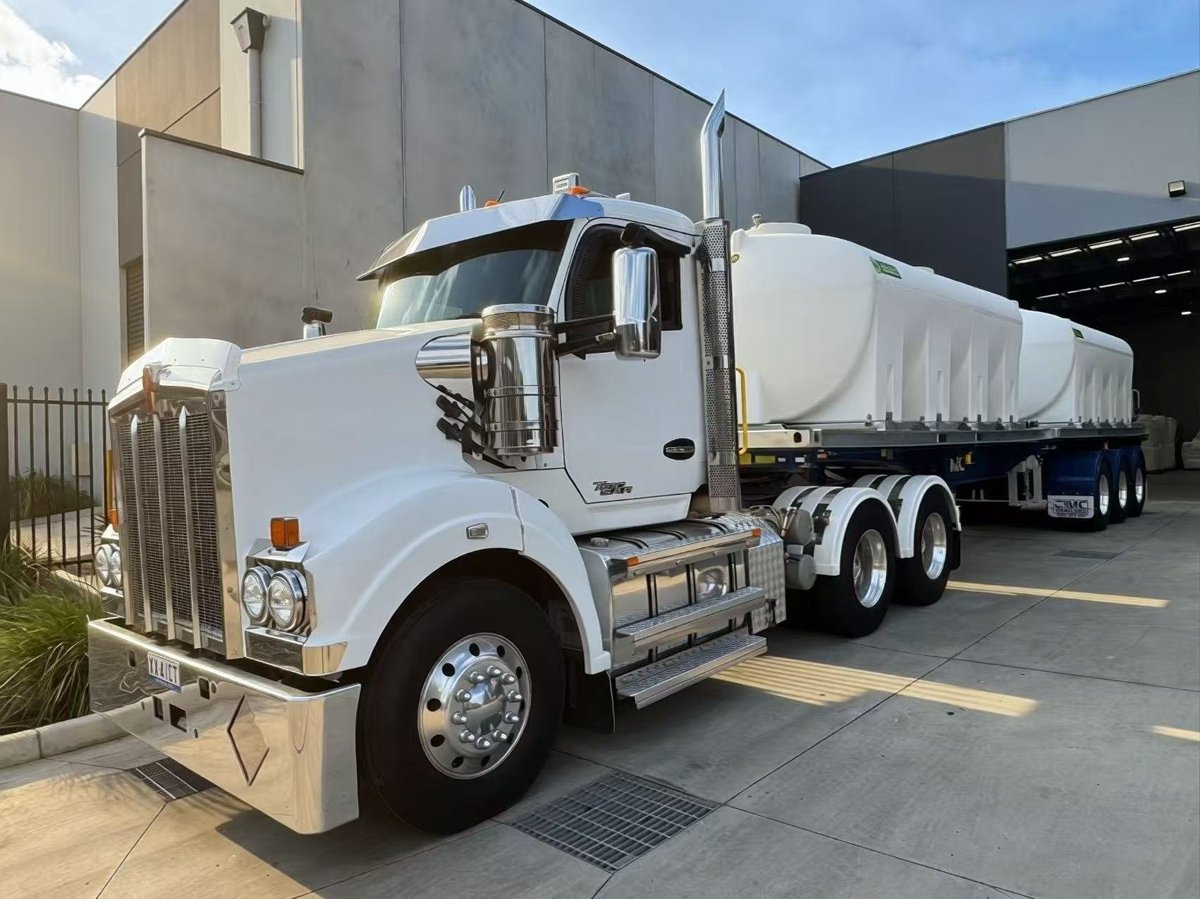 White Peterbilt tanker truck parked at a facility with large tank trailer attached